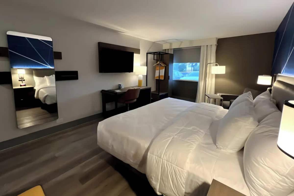 Ein Hotelzimmer mit einem großen Bett, einem Schreibtisch, einem Stuhl, einem Fernseher und einem Spiegel.