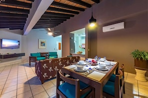 Un comedor con una mesa dispuesta para cuatro personas, un sofá y un televisor al fondo.