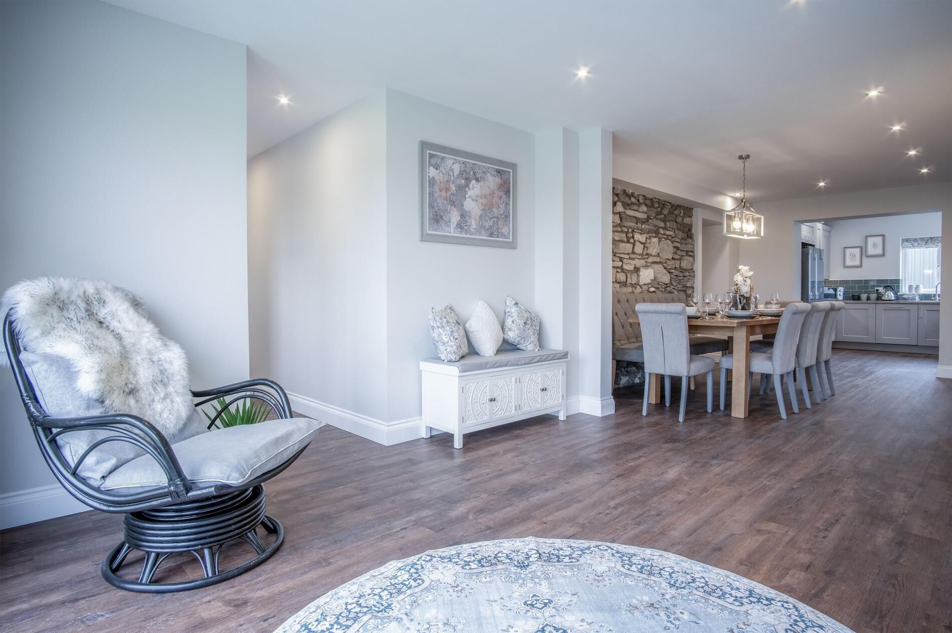 A modern dining area with a round table, grey upholstered chairs, and a white console table with decorative pillows.
