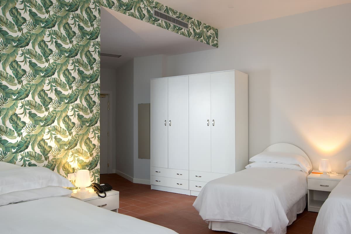 A hotel room with two beds, a wardrobe, a bedside table with a lamp, and a telephone.