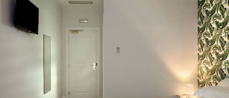 A bedroom with a bed, a nightstand, a wall-mounted TV, a door, and a patterned wallpaper.