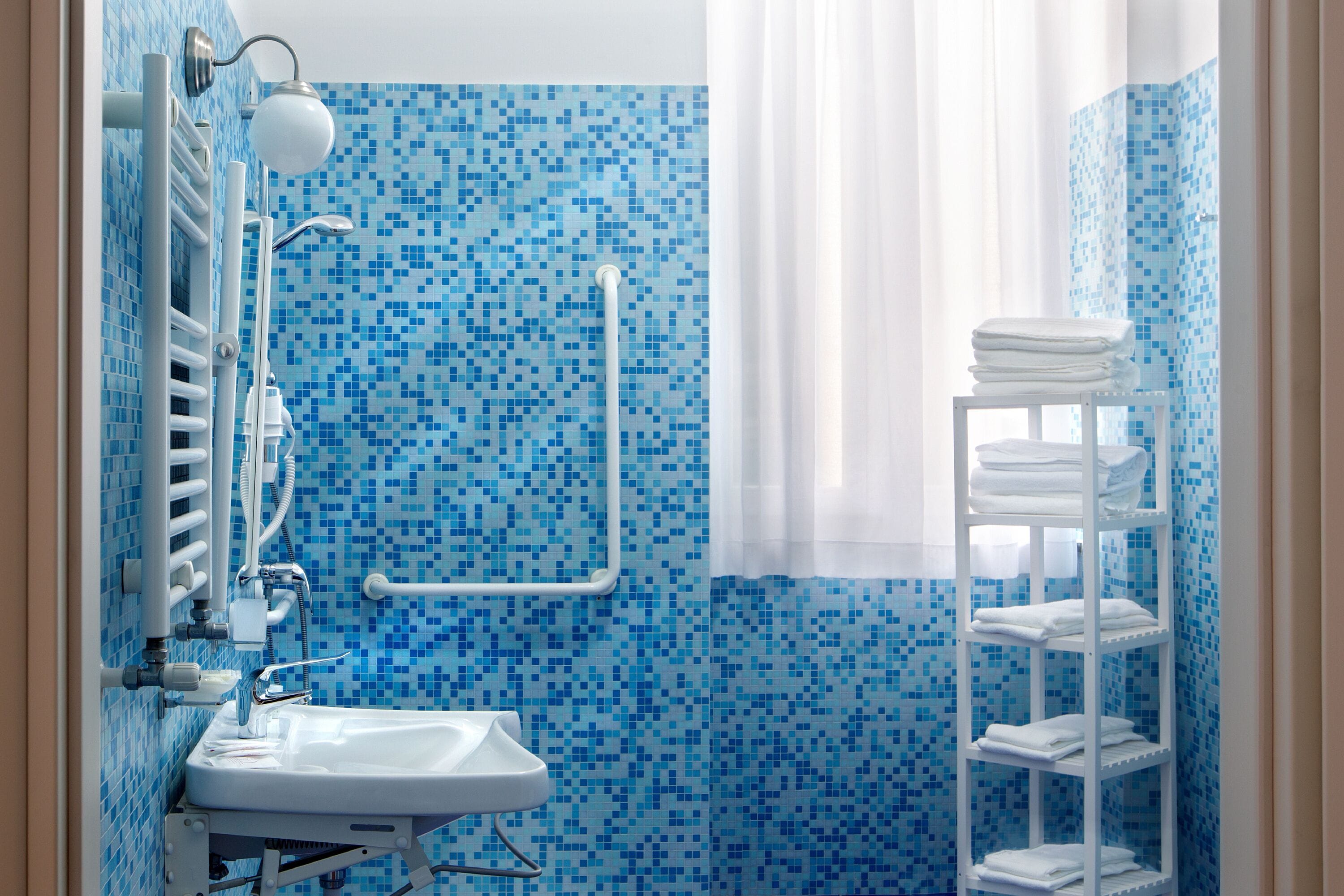 A bathroom with a blue mosaic tile wall, a white sink, a towel rack, and a shower area.