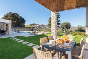 A patio with a table set for breakfast, a pool, and a stone wall.