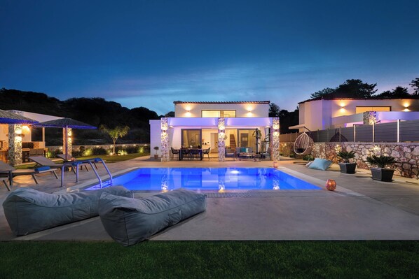 A modern house with a swimming pool, outdoor seating, and a stone wall.