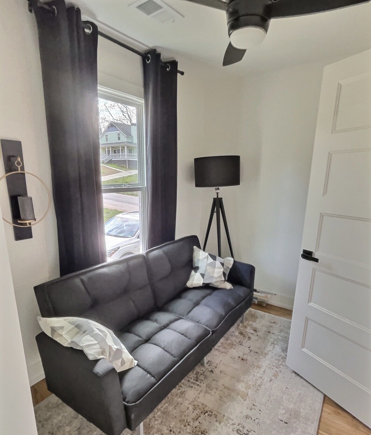A modern living room with a black leather sofa, a floor lamp, and a view of the outside.
