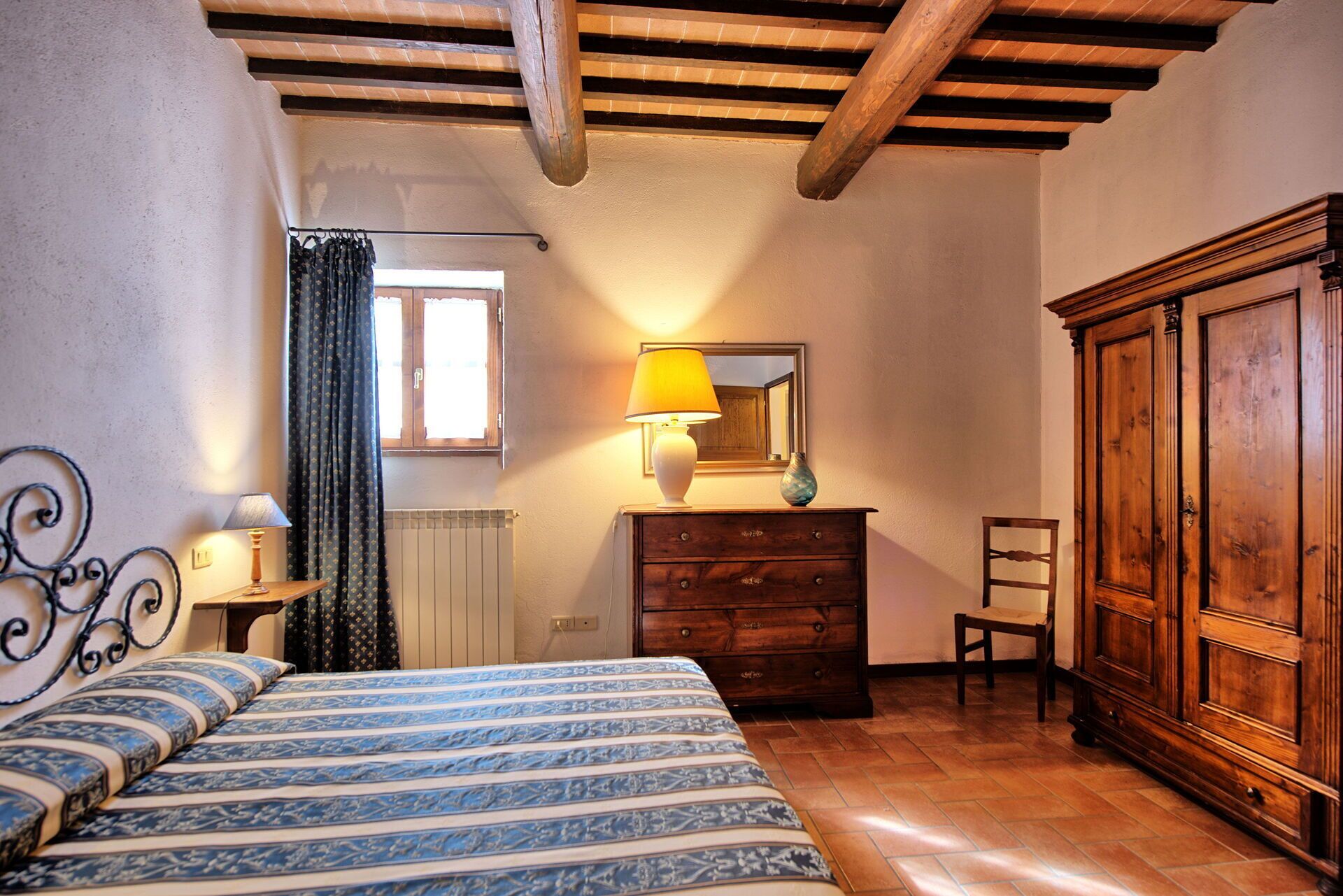 Ein Schlafzimmer mit Bett, Schminktisch, Stuhl, Heizkörper und einem Fenster mit Vorhängen.