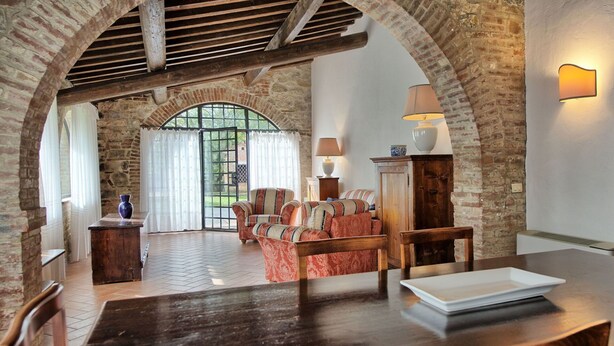 Un interior rústic amb arcs de maó descobert, una taula de fusta i una zona d'ambientació amb coixins estampats.