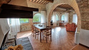 Una àmplia zona de dinar amb taula i cadires de fusta, parets de pedra i grans finestres.