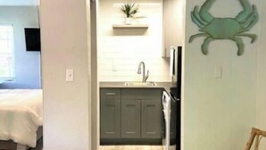 Un espacio habitable compacto con kitchenette, un comedor con sofá azul y un adorno de cangrejo colgado en la pared.