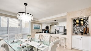 A modern kitchen with white cabinetry, a black backsplash, and a dining area with a glass table and white chairs. - Beachfront |Pool, Games, No Stairs! Sleeps 12 (Destin)