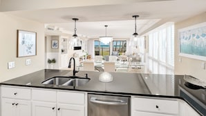 A modern kitchen with a central island, stainless steel appliances, and a view to the living area. - Beachfront |Pool, Games, No Stairs! Sleeps 12 (Destin)