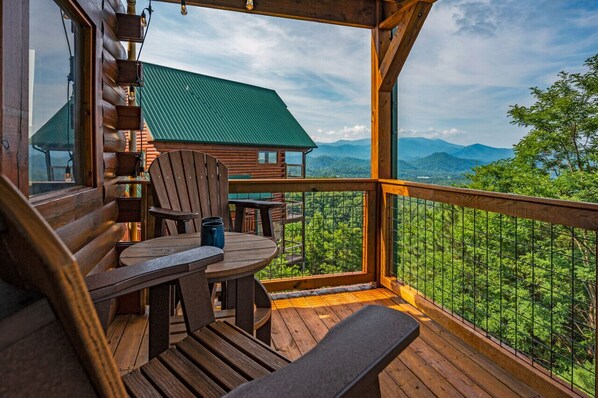 Terraza de madera con mesa y sillas, con vistas a un paisaje montañoso.