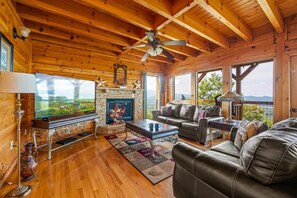 Interior de una cabaña de madera con chimenea, sofá de cuero y televisor.