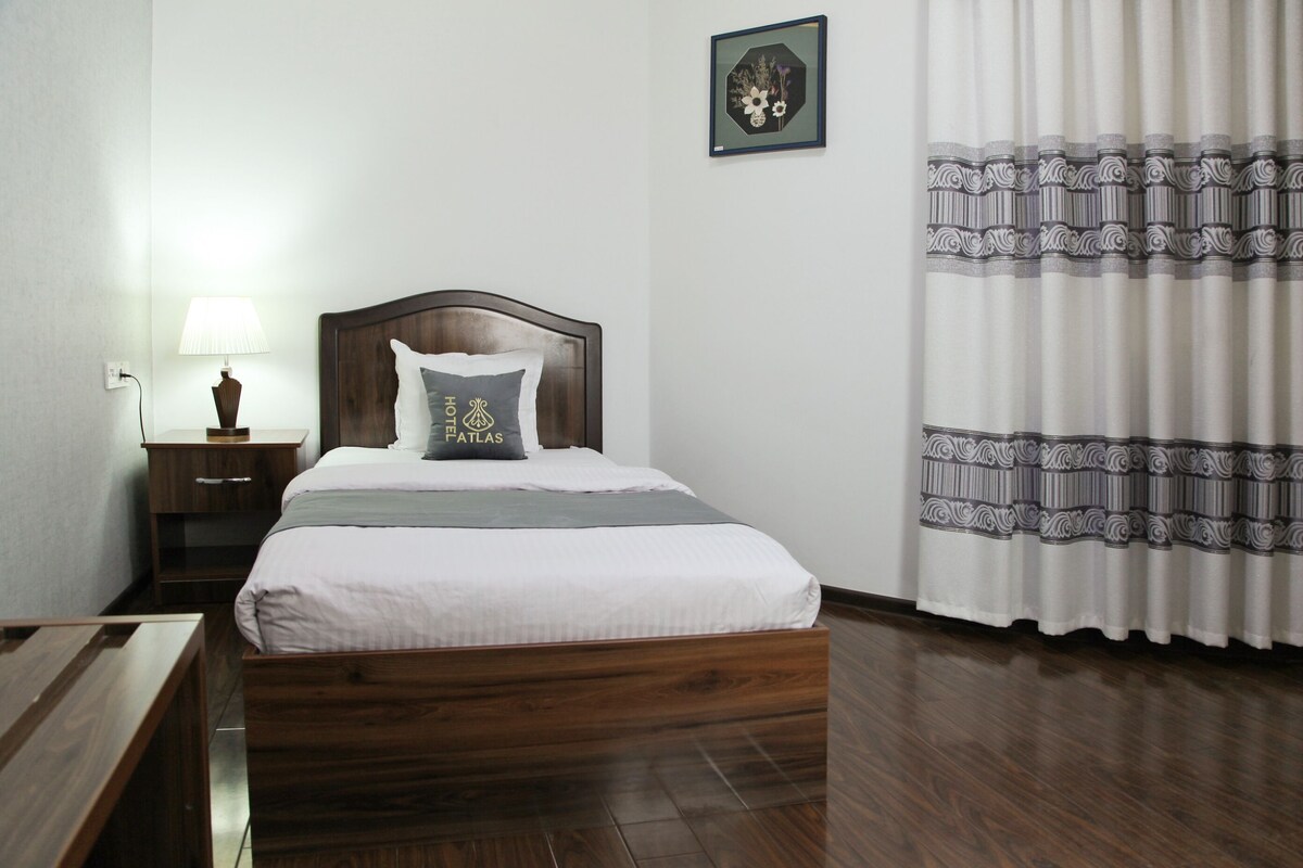 A neatly arranged bedroom with a wooden bed, a nightstand with a lamp, and a framed picture on the wall.