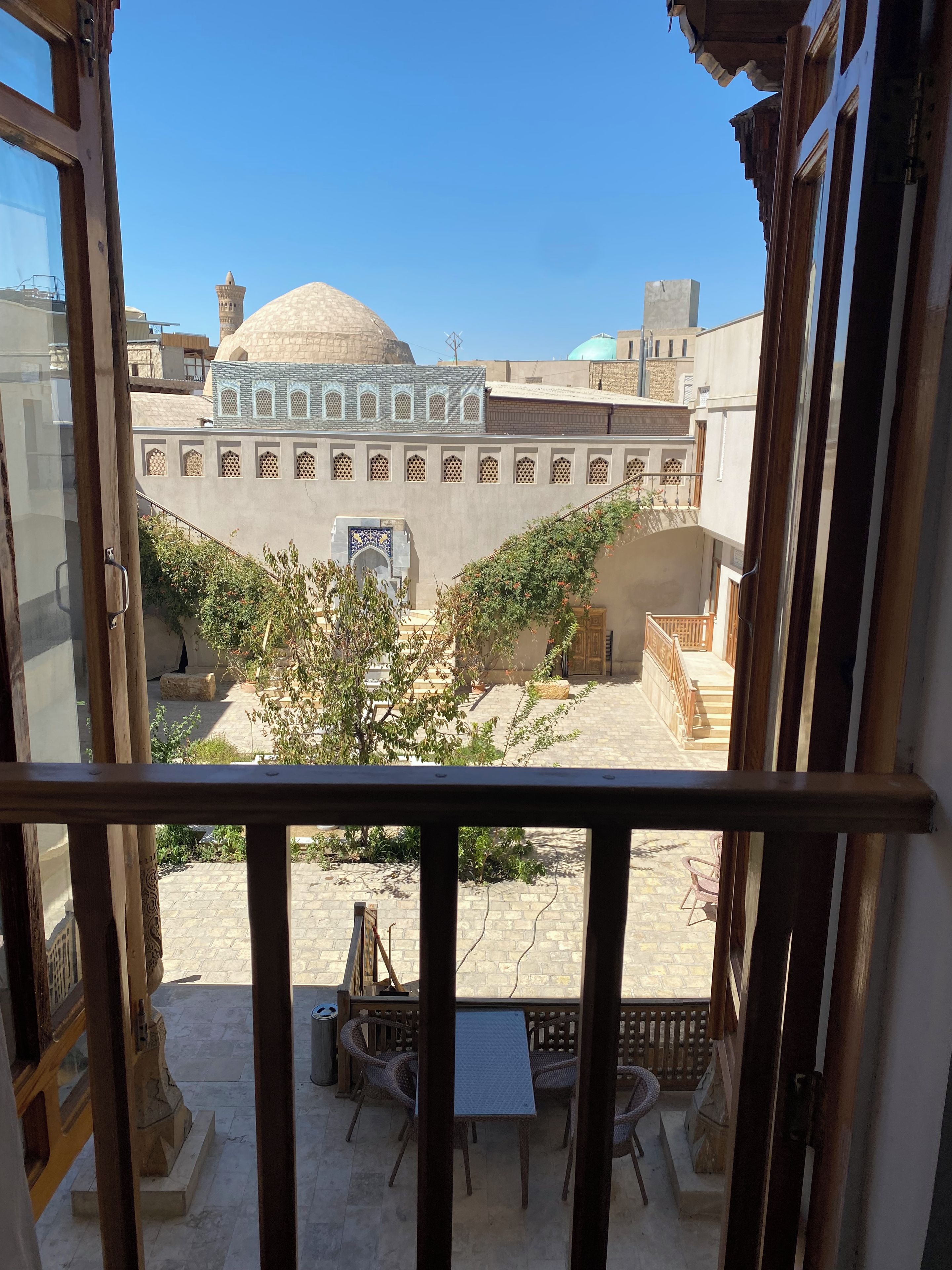 Blick von einem Balkon mit Tisch und Stühlen, ein kleiner Garten und ein Gebäude mit einer Kuppel und Bogenfenstern.