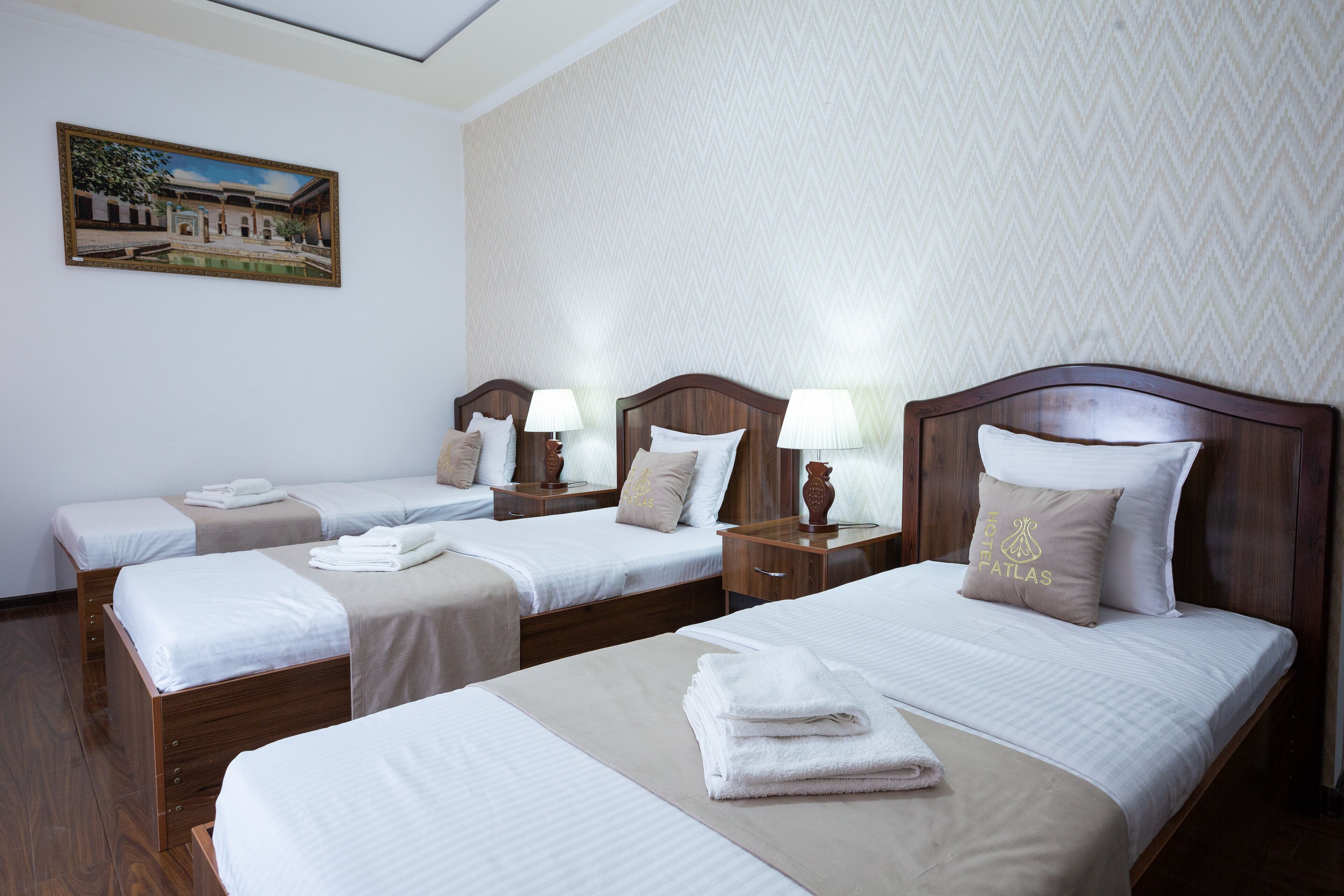 A hotel room with three single beds, each with a wooden headboard, white linens, and a lamp on a bedside table.