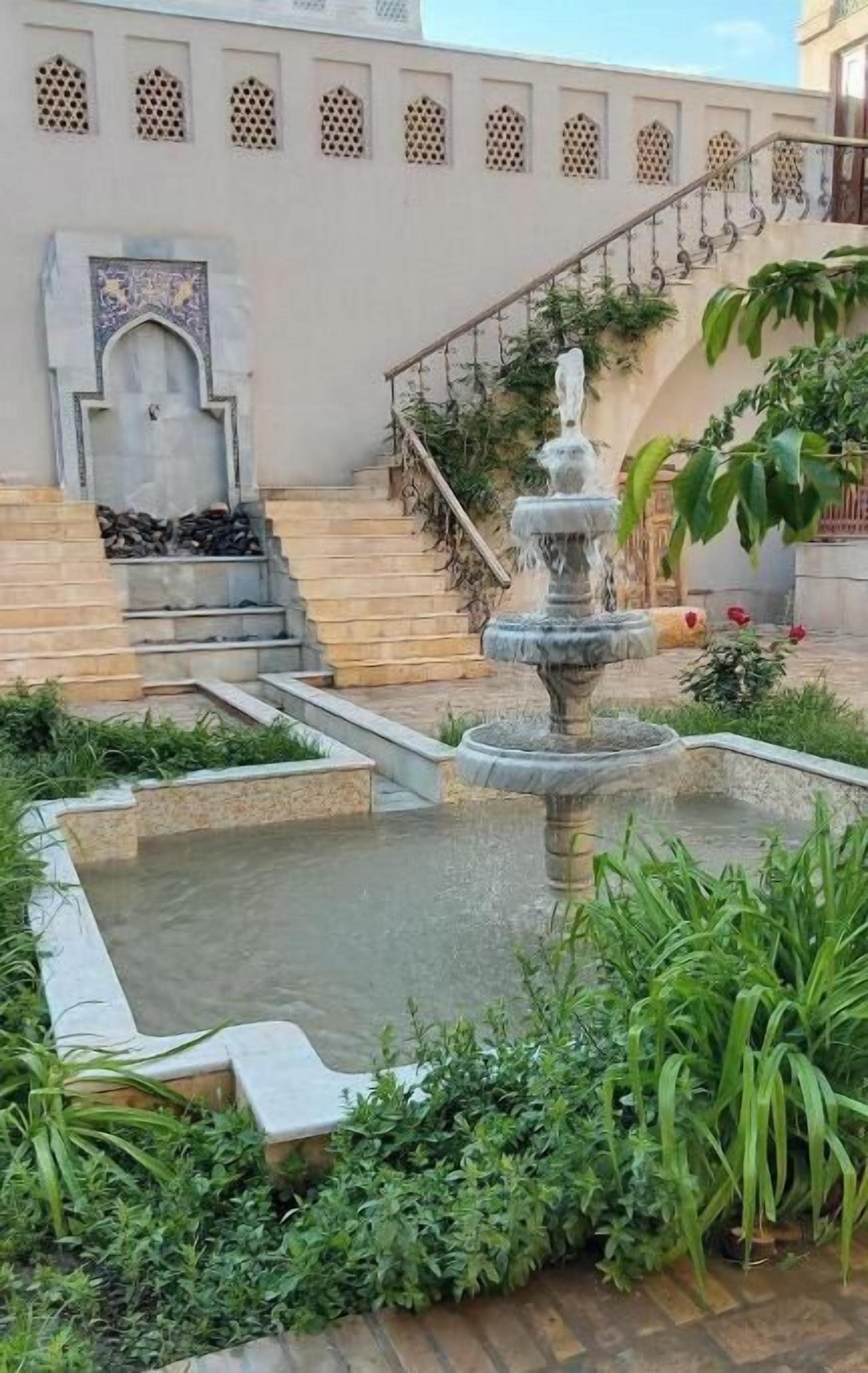 Un patio con una fuente, una escalera y un muro con detalles decorativos.