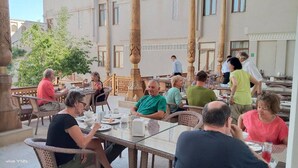 Ein Essbereich im Freien mit Korbstühlen und Tischen, umgeben von Säulen und einem Gebäude mit traditioneller Architektur.