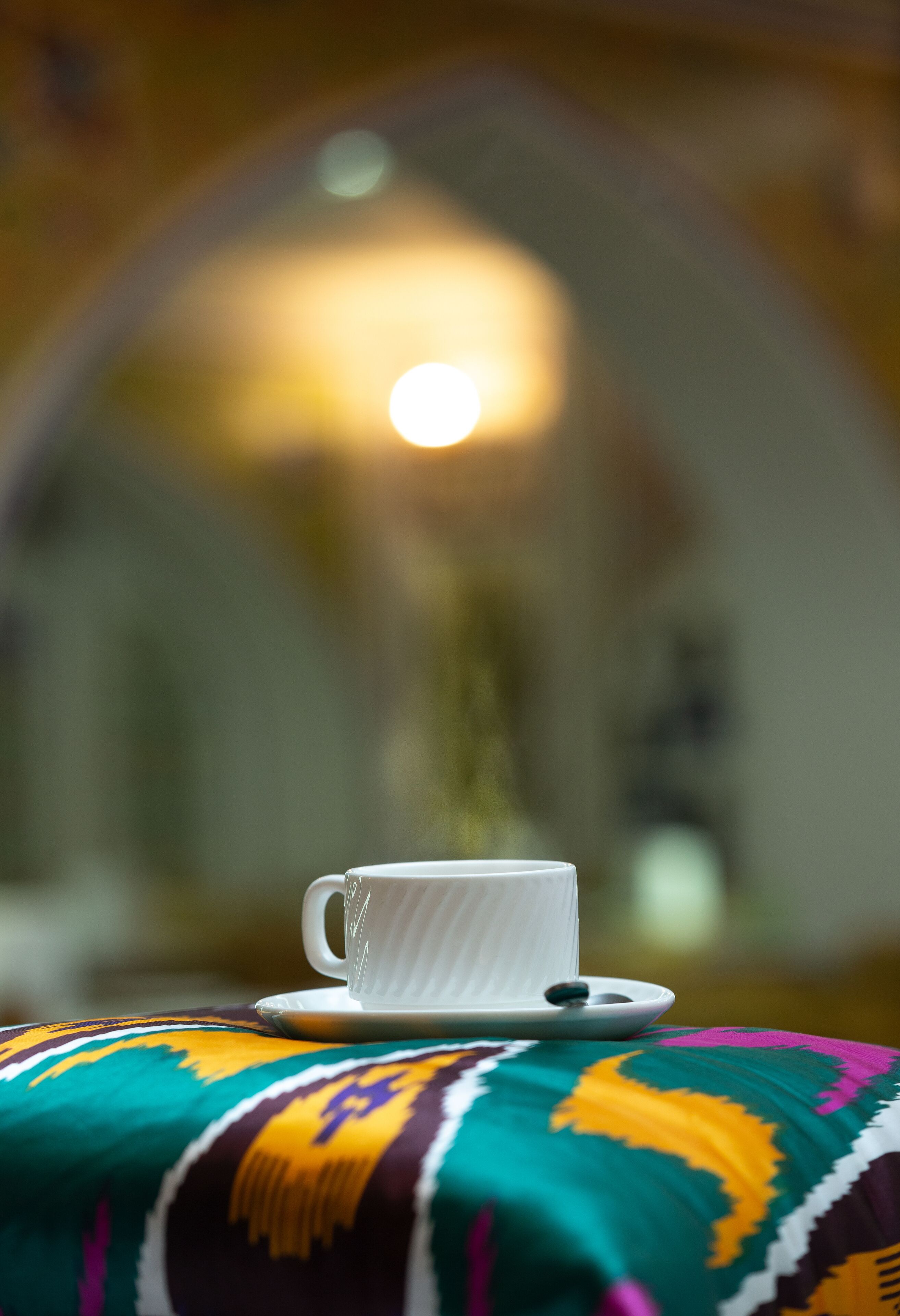 A white cup on a saucer on a colorful cushion.