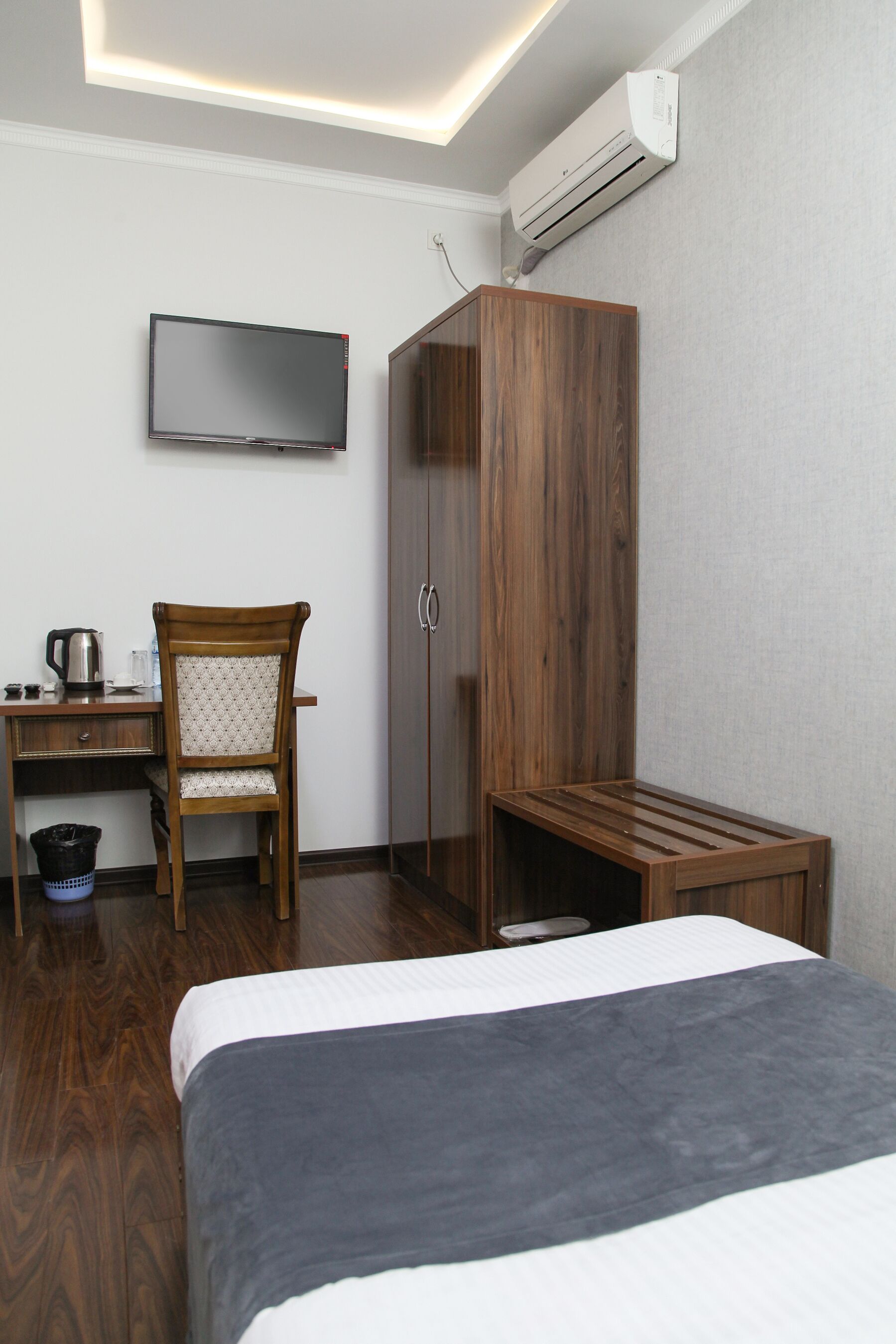 A hotel room with a bed, a desk with a chair, a television, and a wardrobe.