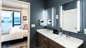 A modern bathroom with a large mirror, two sinks, and a window with a view of buildings. - Glam Downtown Retreat w/ Pool | Girls’ Trips & Bachelorettes | Sleeps 8 (Nashville)