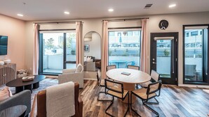 A modern living room with a round wooden table, comfortable seating, and large sliding glass doors leading to a balcony with outdoor furniture. - Glam Downtown Retreat w/ Pool | Girls’ Trips & Bachelorettes | Sleeps 8 (Nashville)