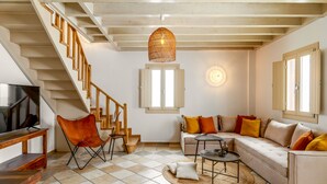 Una sala de estar con sofá, mesa de centro, sillón, televisor y escalera.