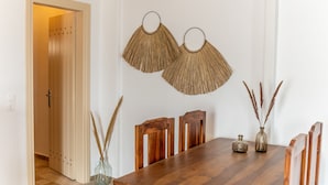 Un comedor con una mesa de madera, dos sillas de madera, un florero con plantas secas y dos elementos decorativos colgados en la pared.