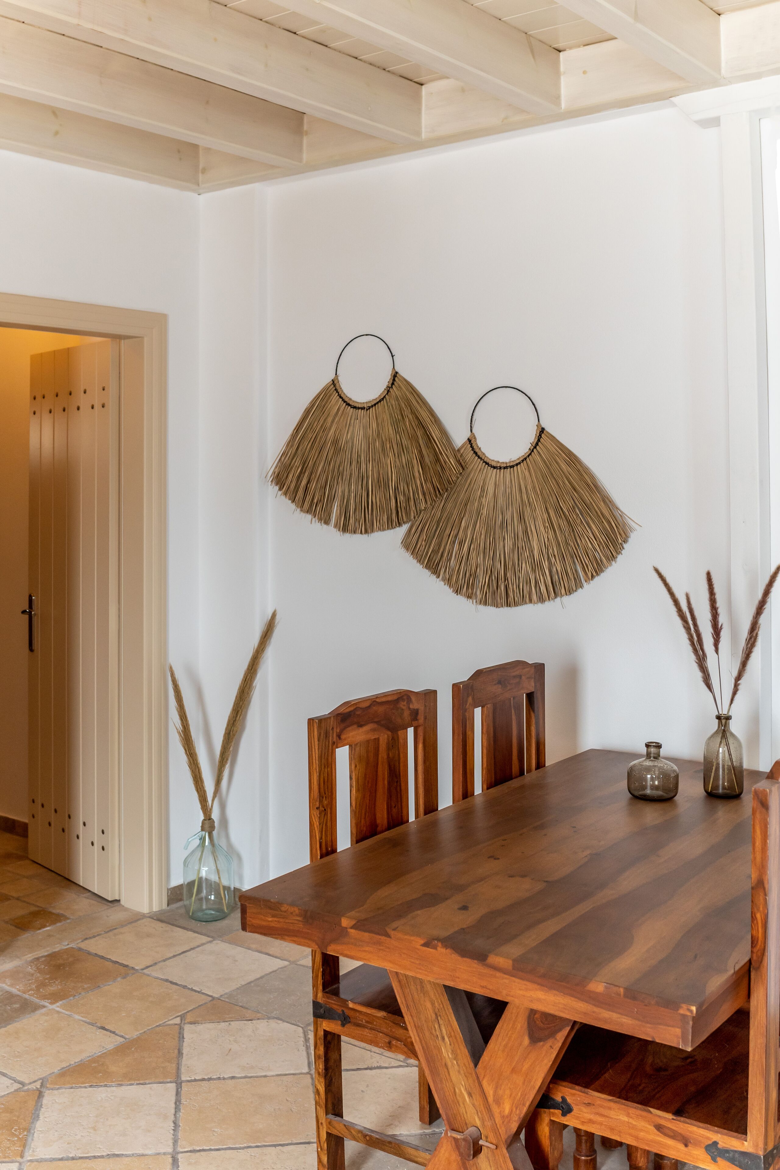 A wooden dining table with chairs, a vase with dried plants, and two wall-mounted fans.