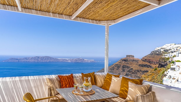Una terraza con mesa y sillas, vista al mar y edificios blancos en una colina.