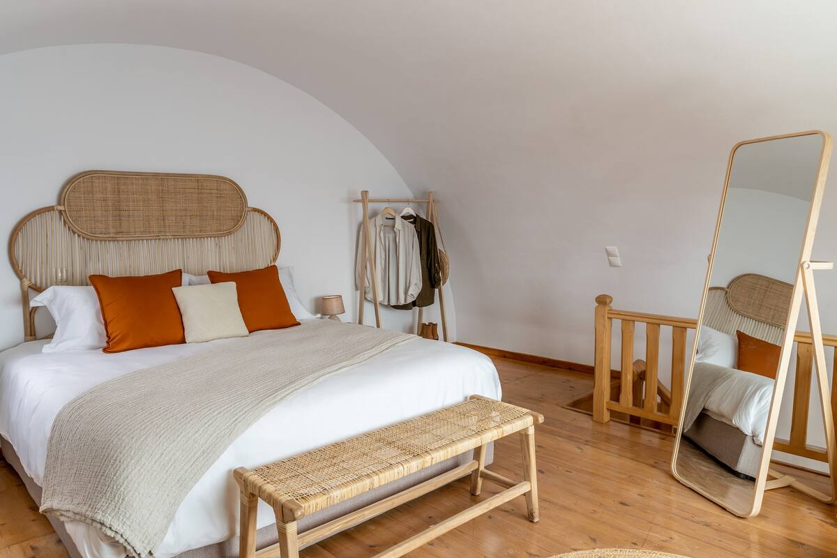 A bedroom with a bed, a bench, a mirror, and a clothing rack.