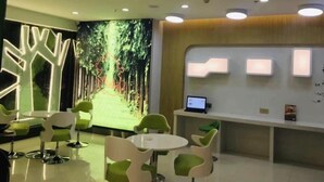 A reception area with a digital screen displaying a forest path, green chairs, a reception desk, and a computer monitor. - Vatica Hefei Anqing West Road Nongda East Gate Hotel (Hefei)