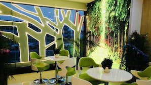A modern interior with green chairs and a white table, a large window, and a wall mural of trees. - Vatica Hefei Anqing West Road Nongda East Gate Hotel (Hefei)