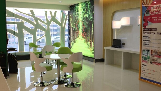 A modern reception area with a digital screen displaying a forest scene, green and white chairs around a table, and a reception desk with a lamp. - Vatica Hefei Anqing West Road Nongda East Gate Hotel (Hefei)