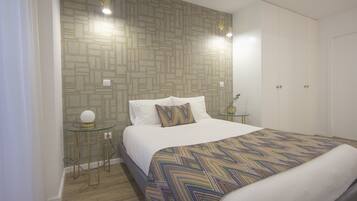 Een moderne slaapkamer met behang met een patroon, een opgemaakt bed met een bontgekleurde deken, nachtkastjes met lampen en een garderobe.
