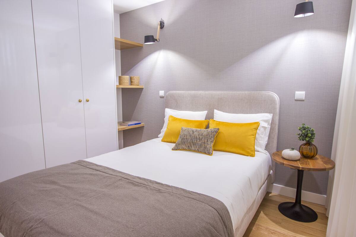 Un dormitorio ordenado con cama, mesita de noche, lámpara y espacio de almacenamiento.