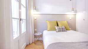 Un dormitorio con una cama, una mesita auxiliar y una ventana con cortinas.