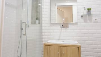 Een moderne badkamer met een glazen douchecabine, een houten wastafelmeubel met een wastafel en een betegelde muur in het wit.