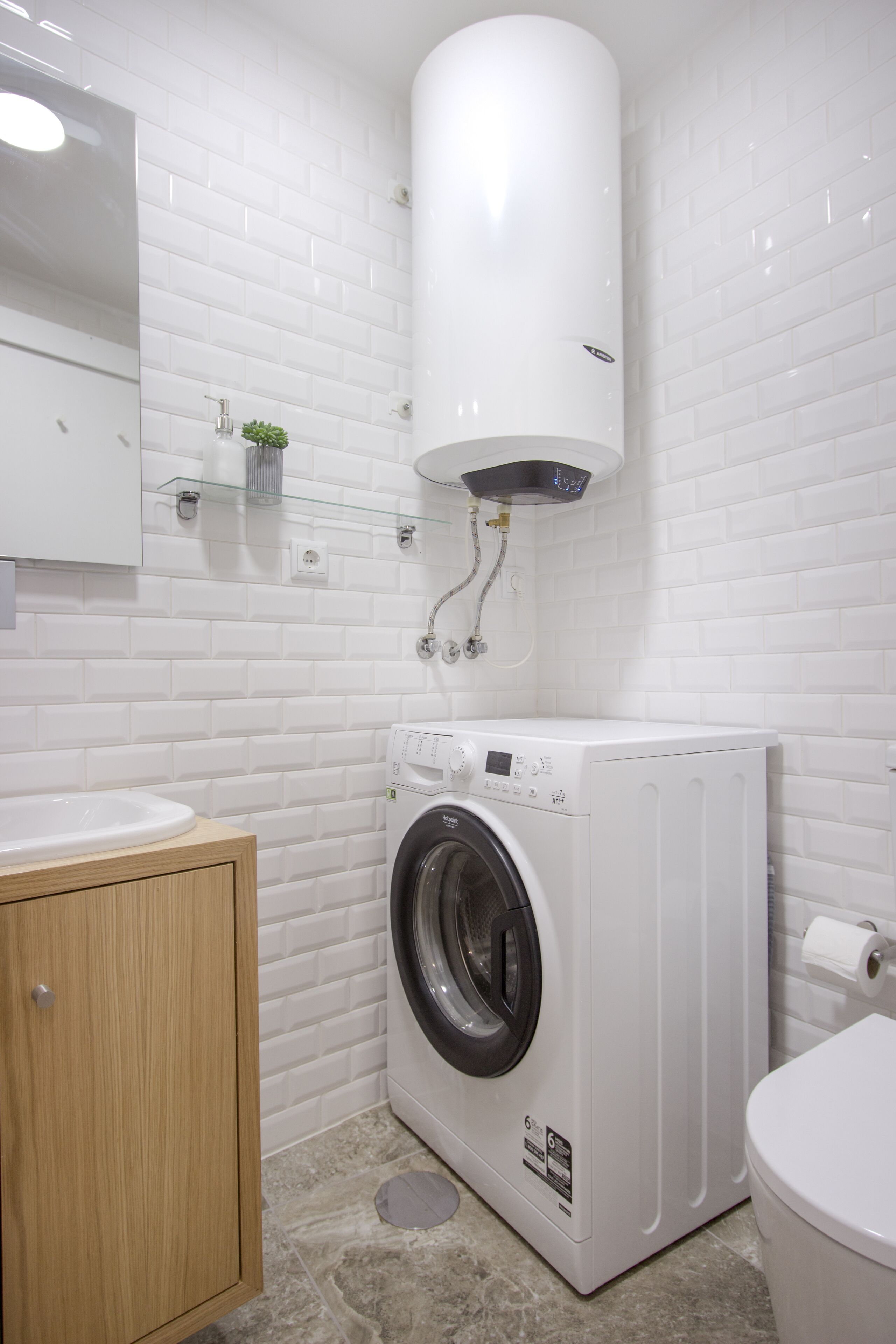 A modern bathroom with white subway tiles, a built-in washing machine, a wooden cabinet, and a toilet.