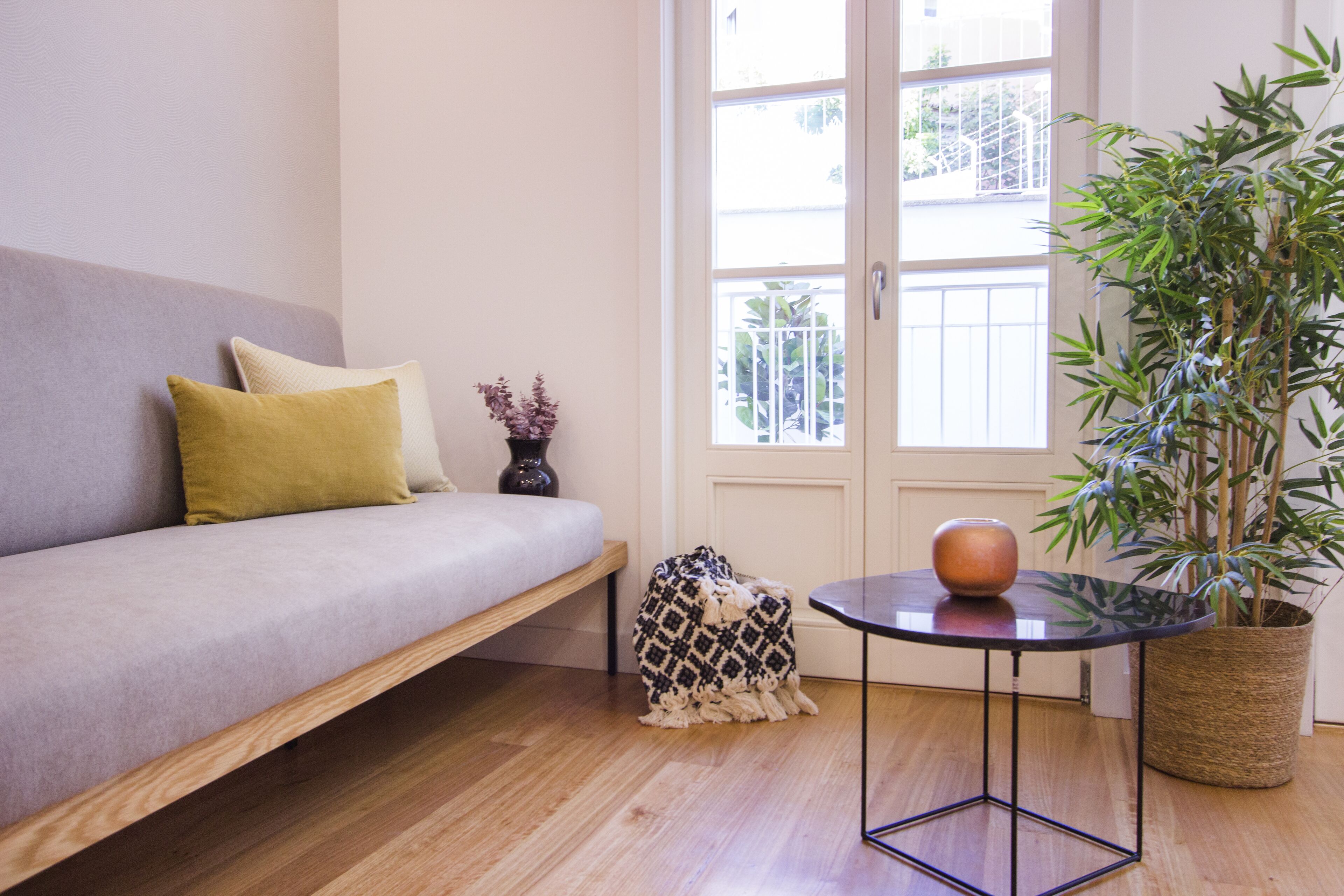 A modern living room with a sofa, a small round table, a potted plant, and a window with a view of the outside.