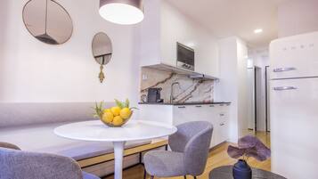 A modern kitchen with white cabinets, a marble countertop, and a built-in oven. There is a dining area with a round table and two chairs.