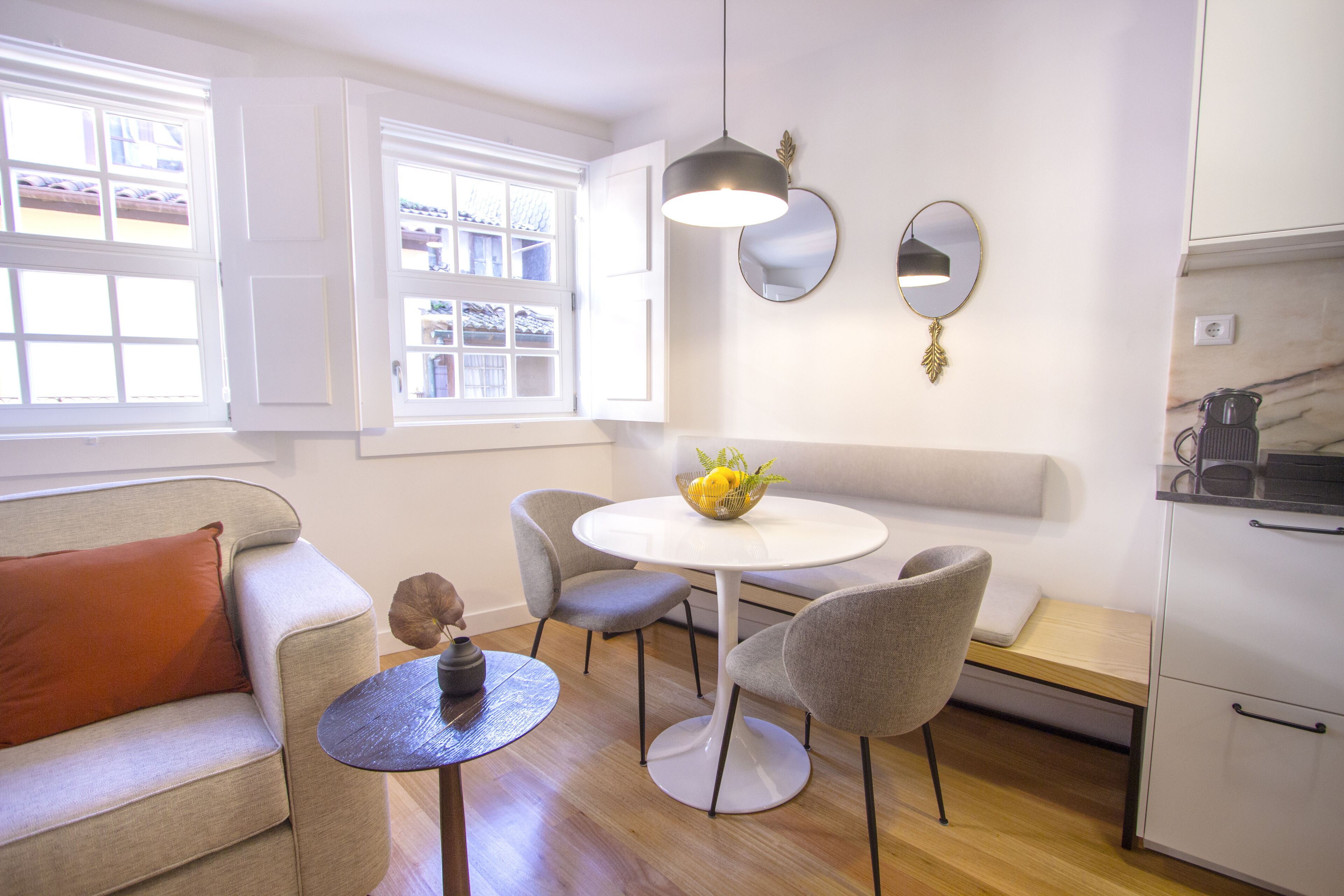 Una sala de estar moderna con un sofá, una mesa redonda con sillas, un cuenco de fruta y una zona de cocina con armarios y una encimera.