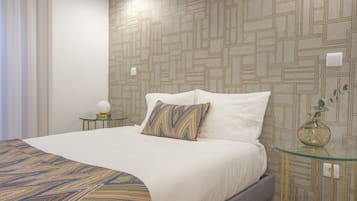 A neatly made bed with a patterned bedspread, a single decorative pillow, and a glass side table with a vase.