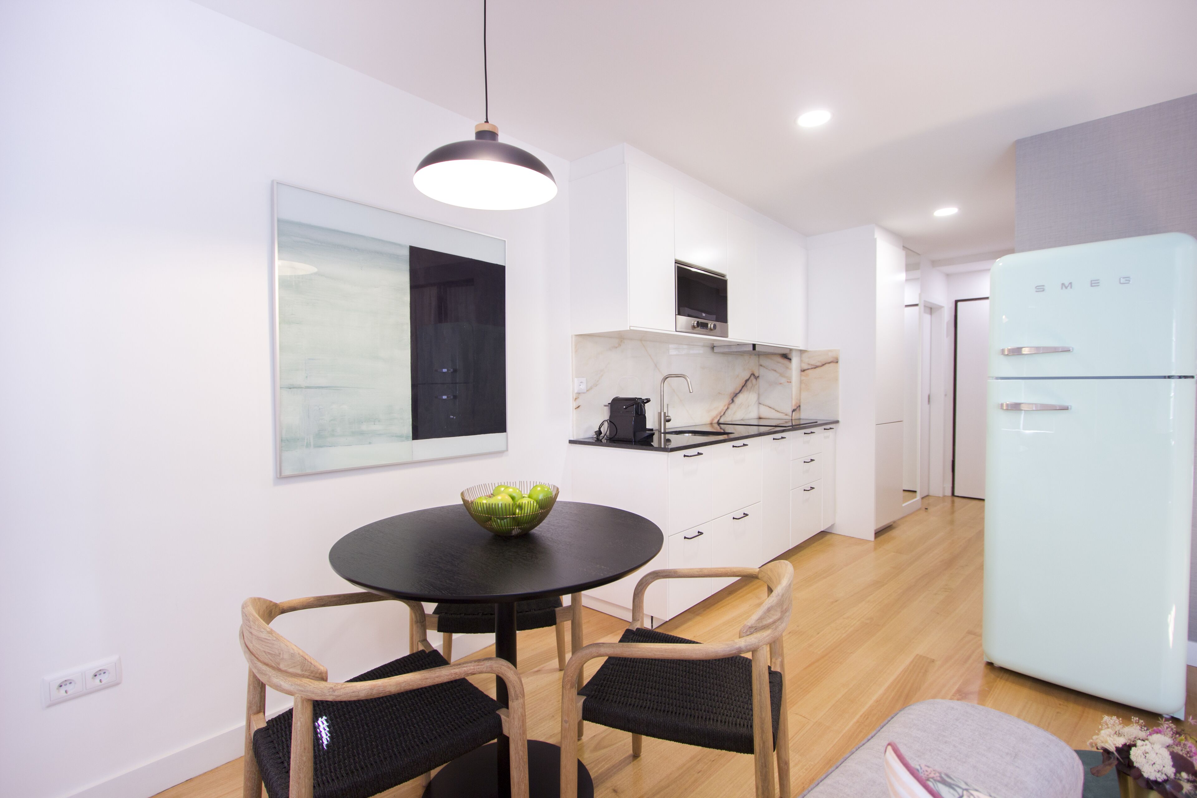 A modern kitchen with white cabinets, a black dining table, and two wicker chairs.