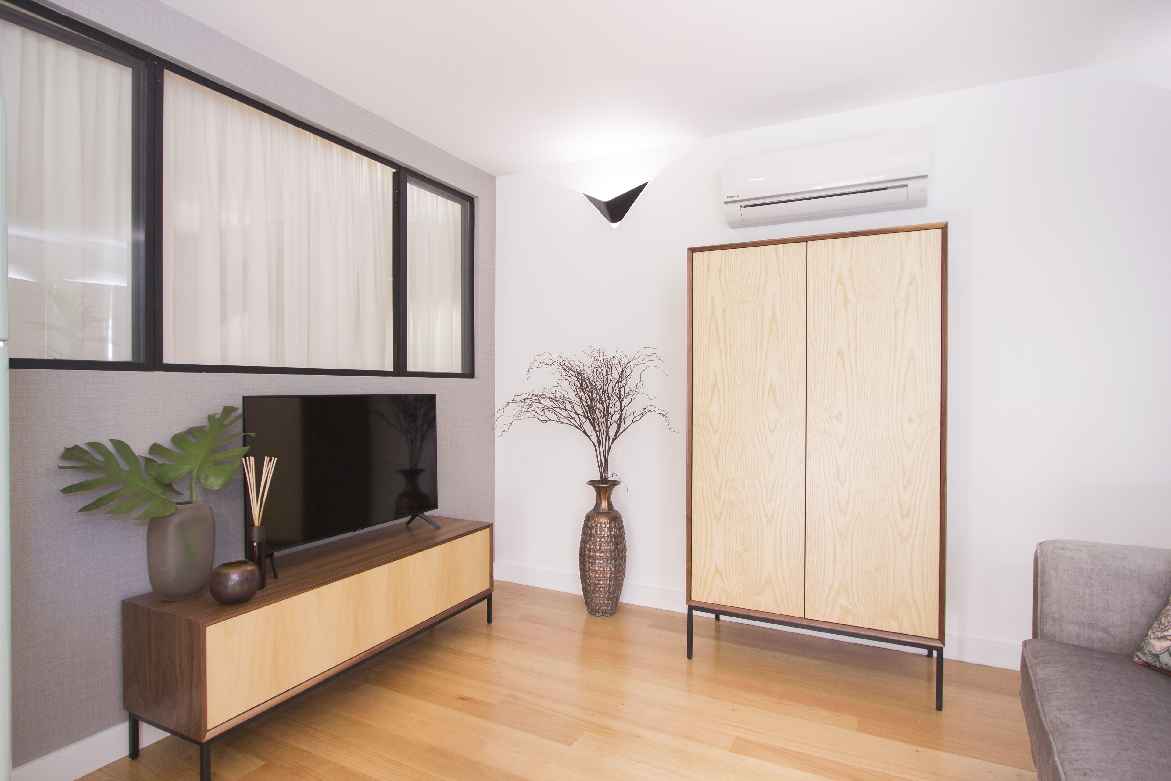 Un salon moderne avec un plancher en bois, un téléviseur posé sur une console en bois, une grande armoire et un vase décoré de branches.