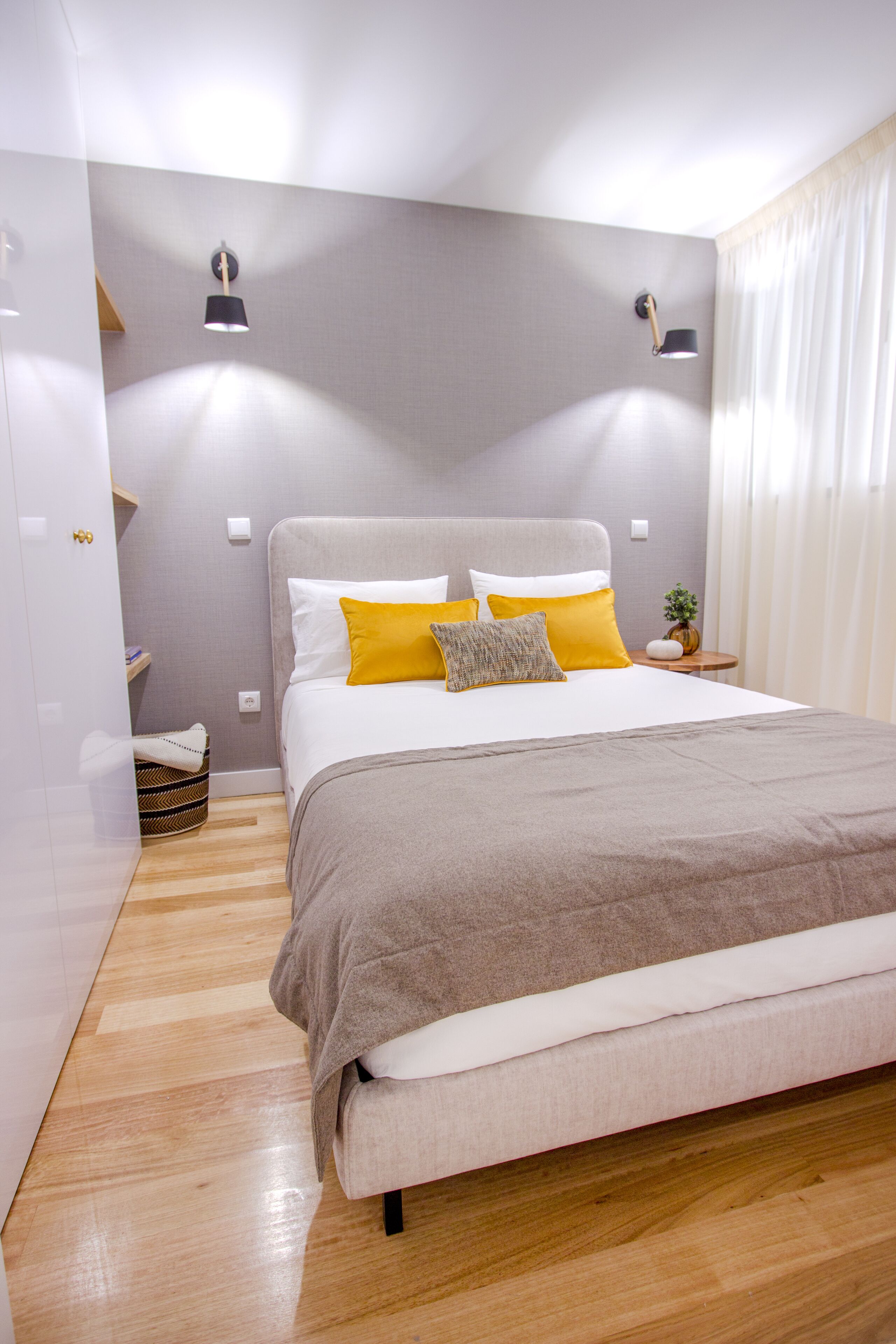 A modern bedroom with a large bed, two bedside lamps, a bedside plant, and a wooden floor.