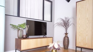 Un salón moderno con un mueble de madera, un televisor de pantalla plana, una mesa redonda de mármol con un florero y un jarrón decorativo alto.