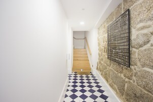 Un pasillo con piso a cuadros, una escalera de madera y una pared de piedra con celosía de metal.