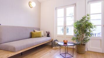 A modern living room with a sofa, a small table, a potted plant, and a window.