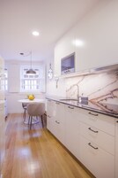 Una cocina moderna con armarios blancos, salpicadero de mármol y horno empotrado.